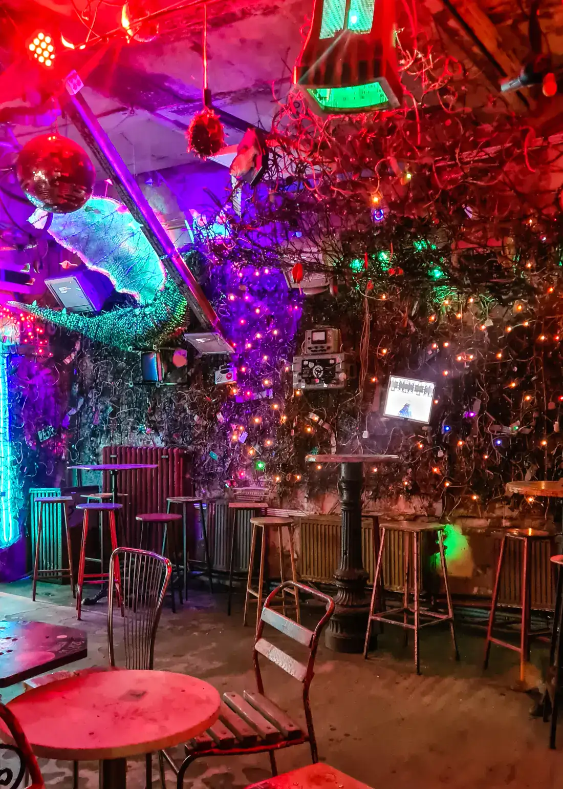 Room inside Szimpla Kert Ruin Bar in Budapest with purple, red and green lights, metal chars and tables.