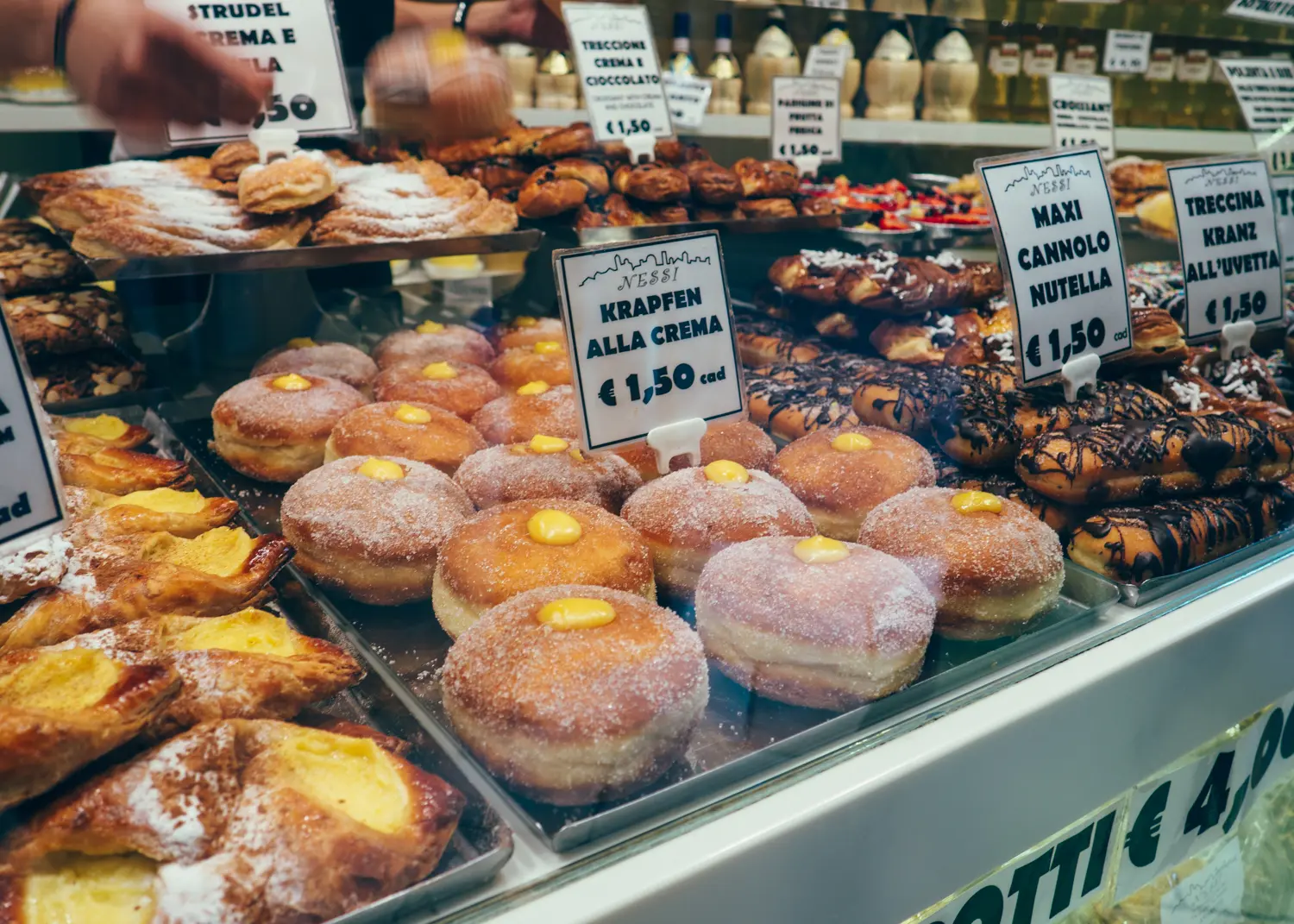 Close up of pastry case with vanilla curd filled donuts and cannoli with white price tags in Bergamo, Italy.