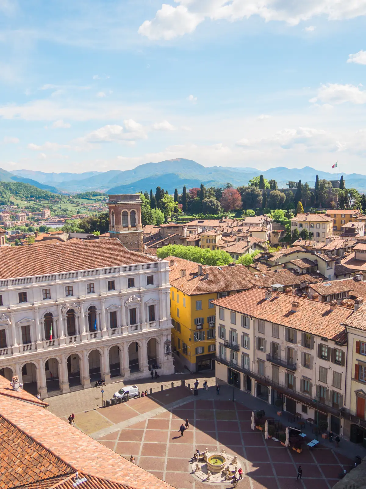Piazza Vecchia, a terracotta colored square surrounded by white and yellow majestic buildings seen from the Civic Tower on a sunny day in Bergamo.