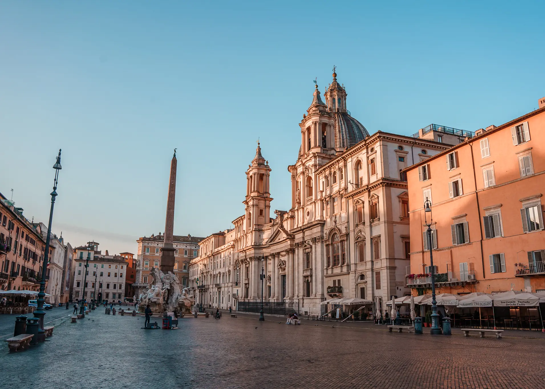 Early morning view of Piazza Navona, surrounded by beige and peach colored stone buildings, in the Historic Centre, one of the best areas to stay in Rome, Italy.