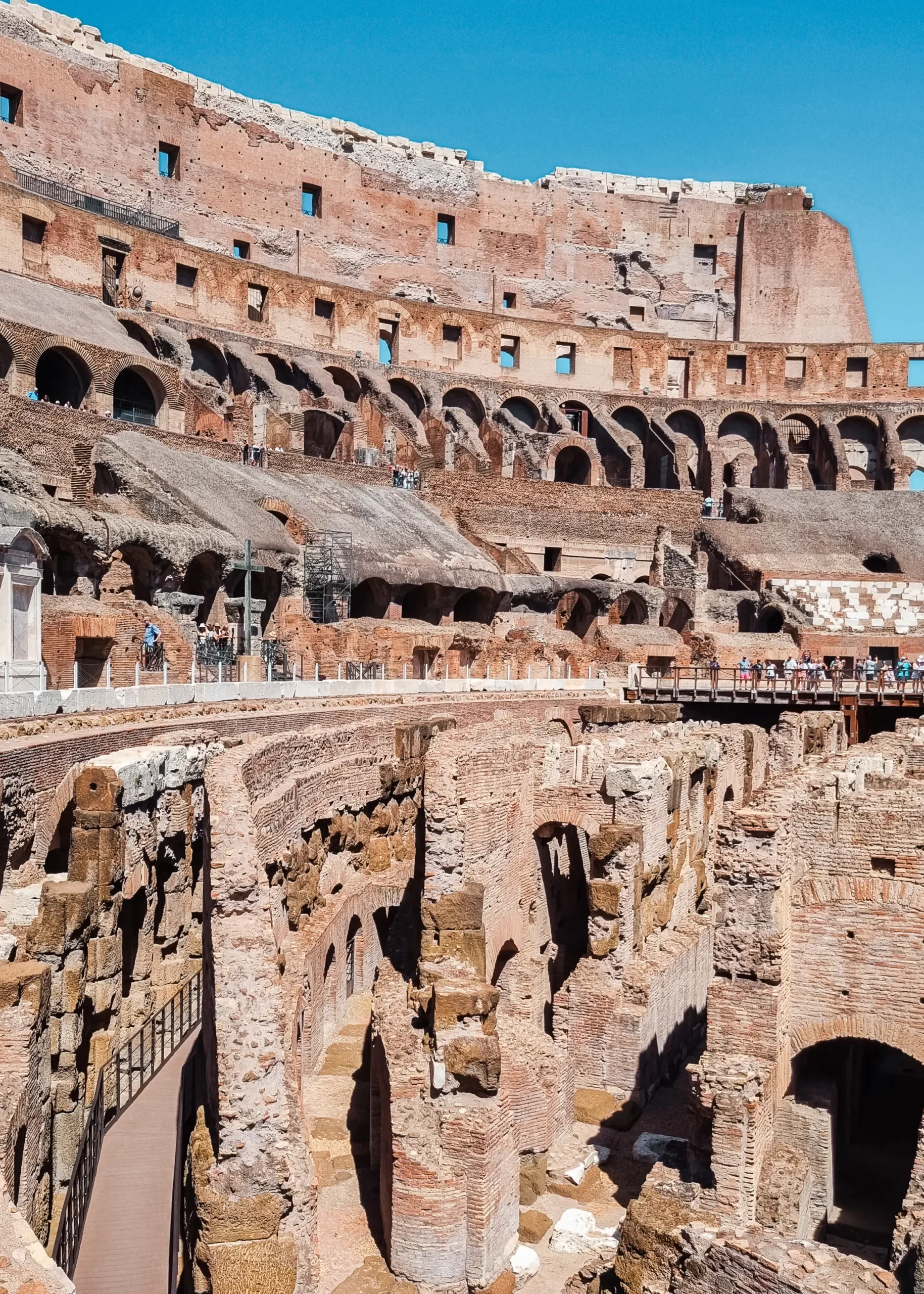 View inside Colosseum of  people walking along the old stone terraces on a sunny day, where to stay in Rome.