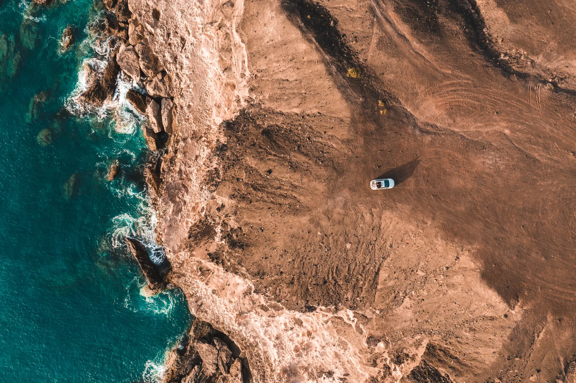 Aerial view of a car parked on a brown cliff the to the blue ocean on Fuerteventura.