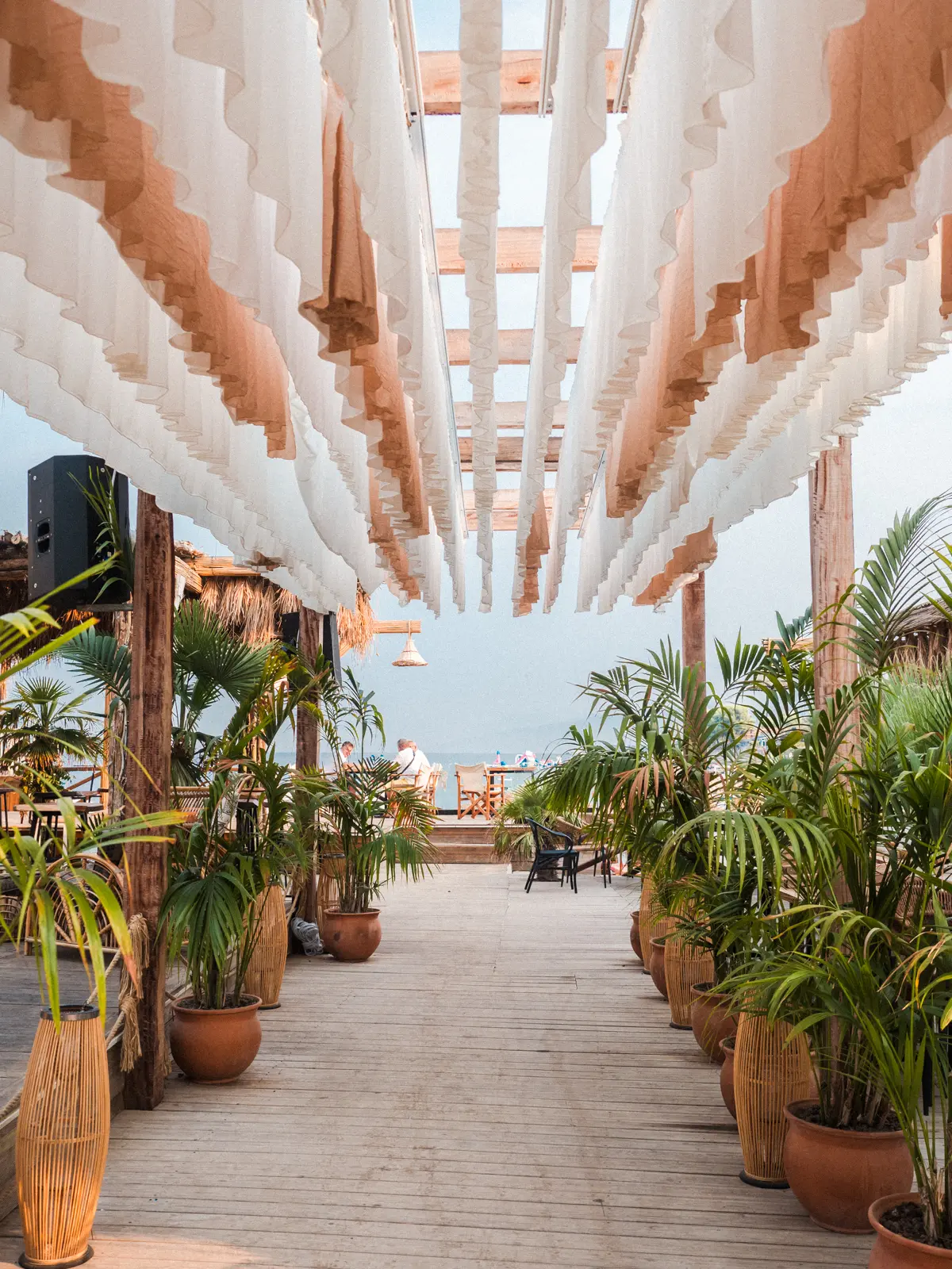 Entrance to Poda Beach Club with flowy white and beige fabrics on the ceiling and green plants in terracotta pots, in Ksamil Albania.