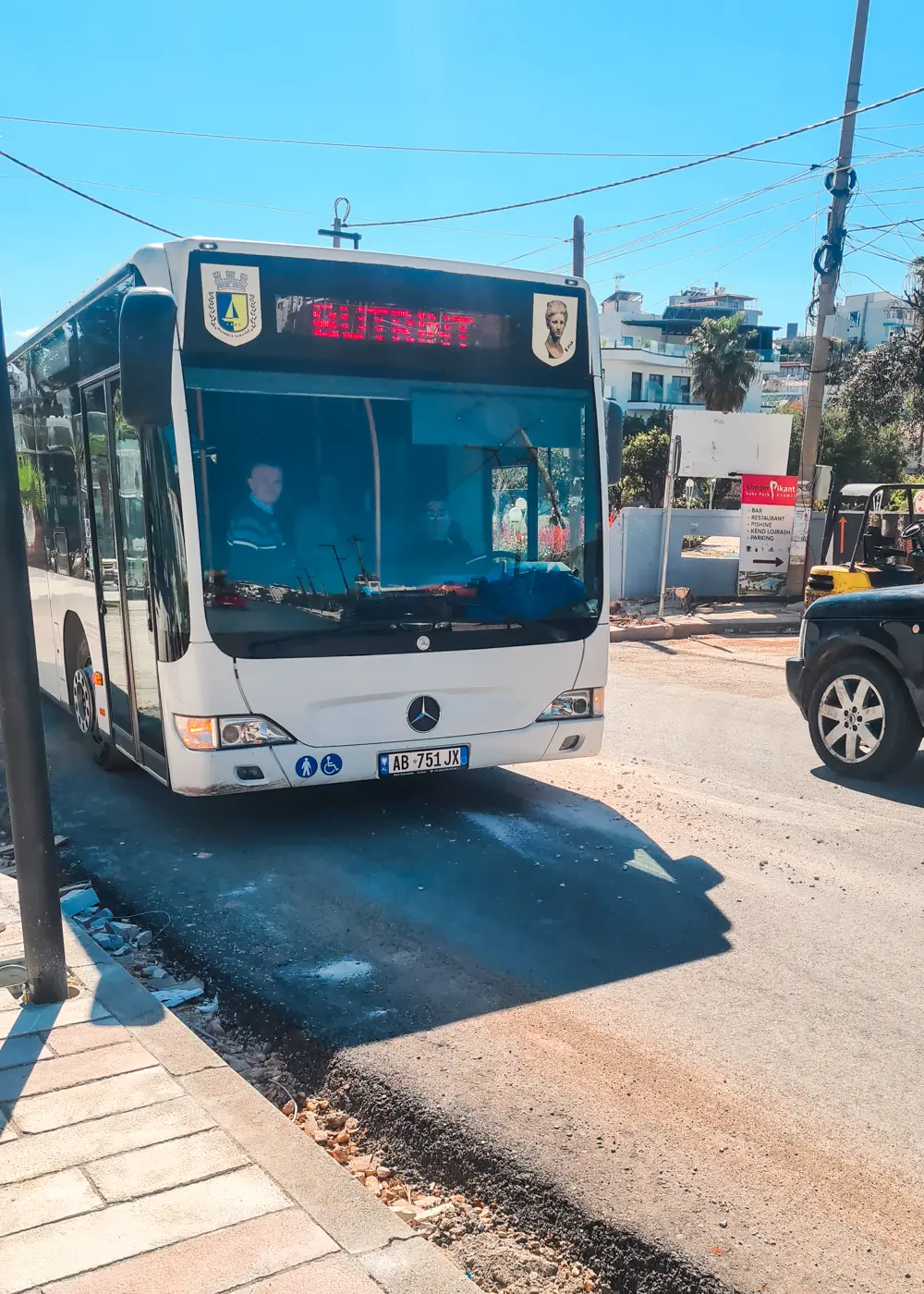 Front of a white bus with red Butrint digital sign, in Ksamil on my way to Saranda.