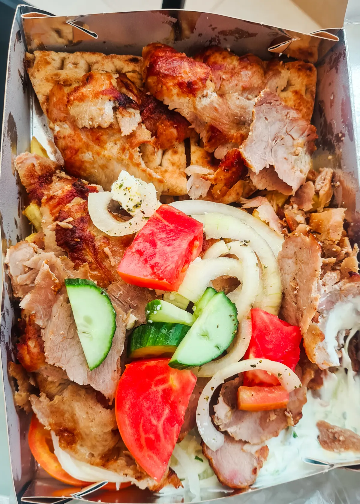 Close up of a takeaway gyro plate with meat, pita bread, cucumber, tomato, onion and tzatziki from Beshiku in Ksamil
