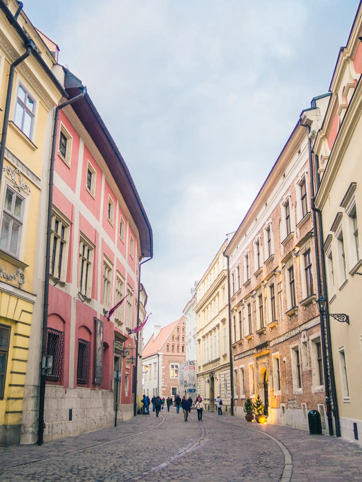 View of the cobbled Kanonicza Street, running between two rows of old houses in beige, yellow and pink, in Krakow Old Town, one of the best places to stay.