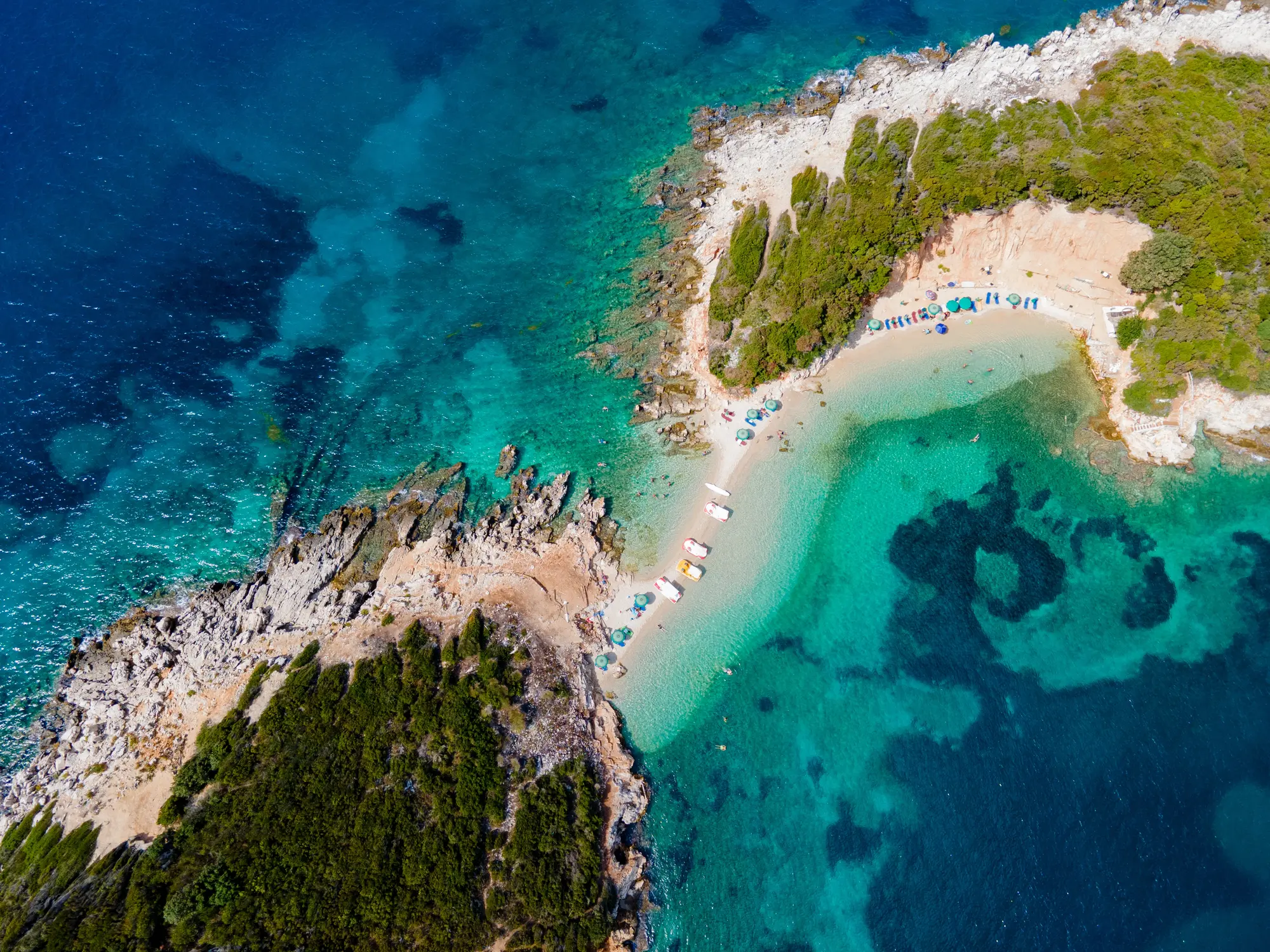 Aerial view of two rocky islets with some greenery connected by a thing strip of sand, in Ksamil.