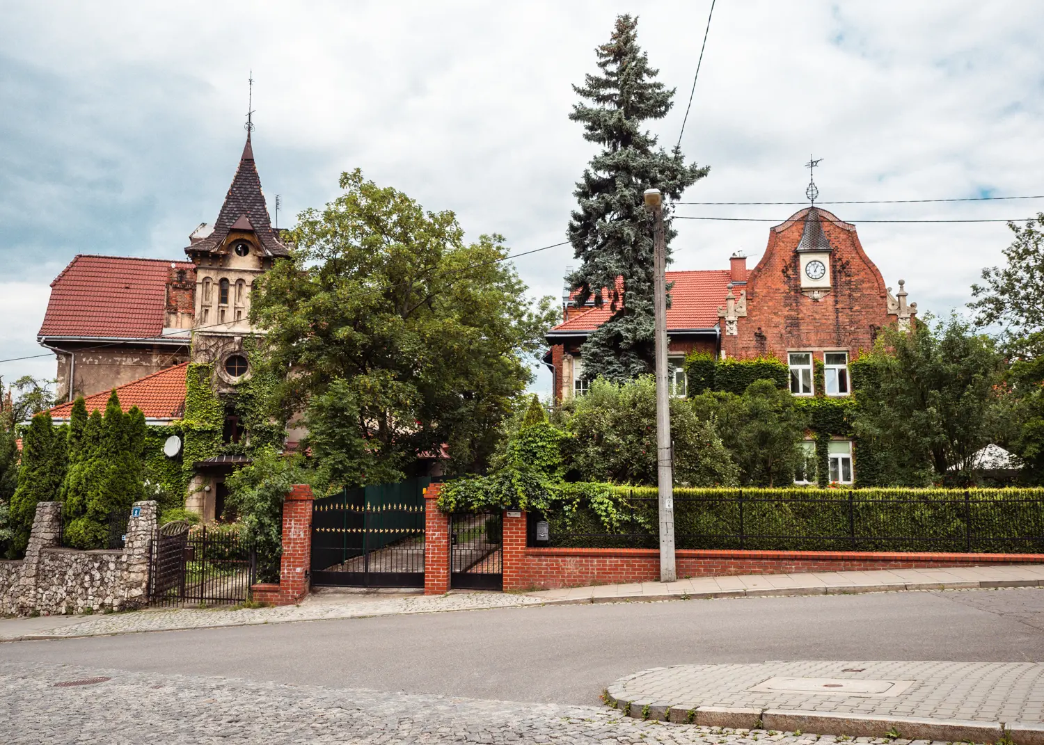 Two unique fairytale-esque villas with orange roofs, behind greenery and gates along a street in Podgorze, one of the more affordable areas to stay in Krakow.