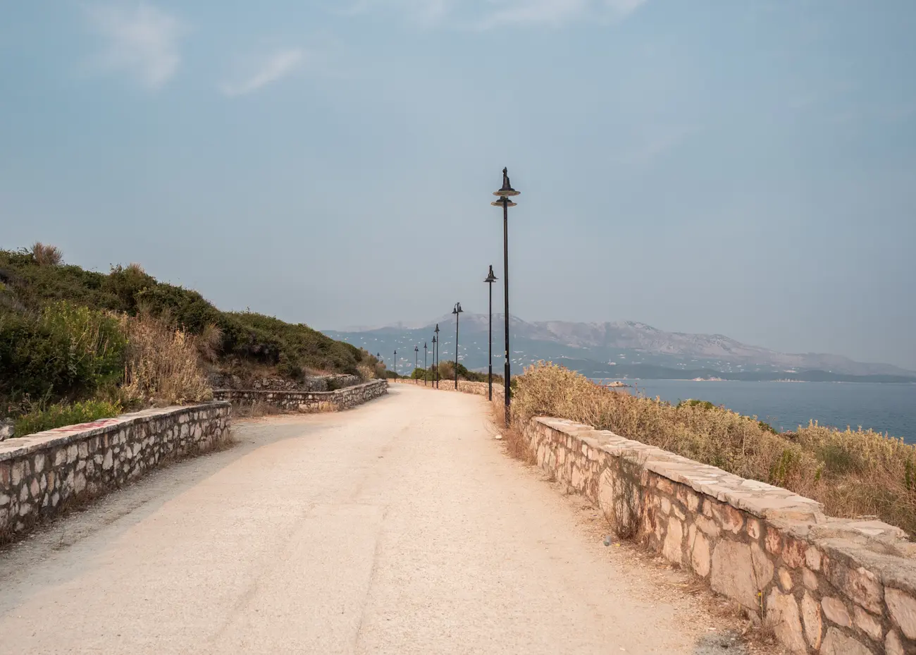 Promenade along the coast in Ksamil lined by stone walls and black street lights.