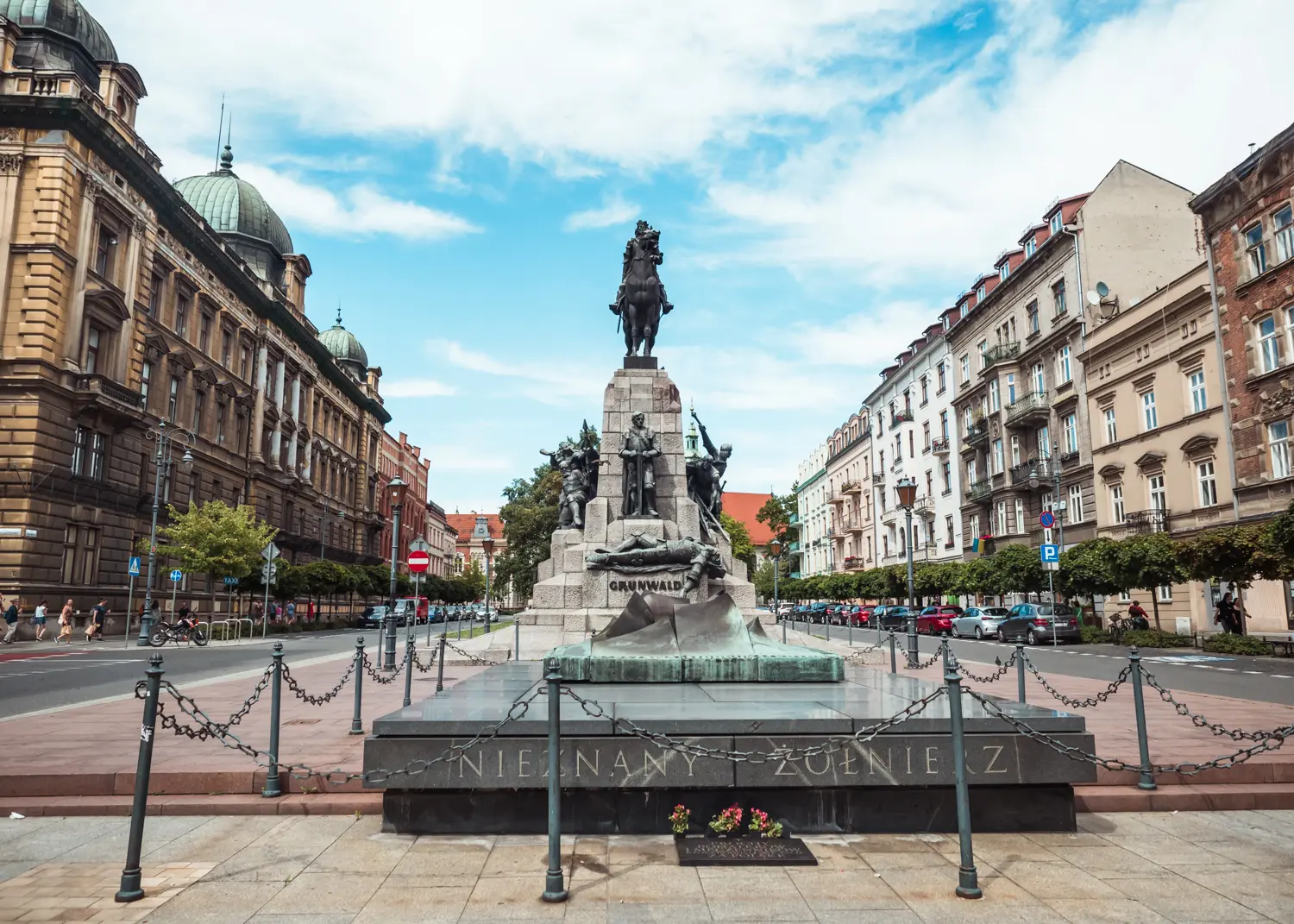Large statue of a man on a horse, with smaller states of people around the base, in the middle of a square in Kleparz with old apartment buildings surrounding it, one of the best places to stay in Krakow.