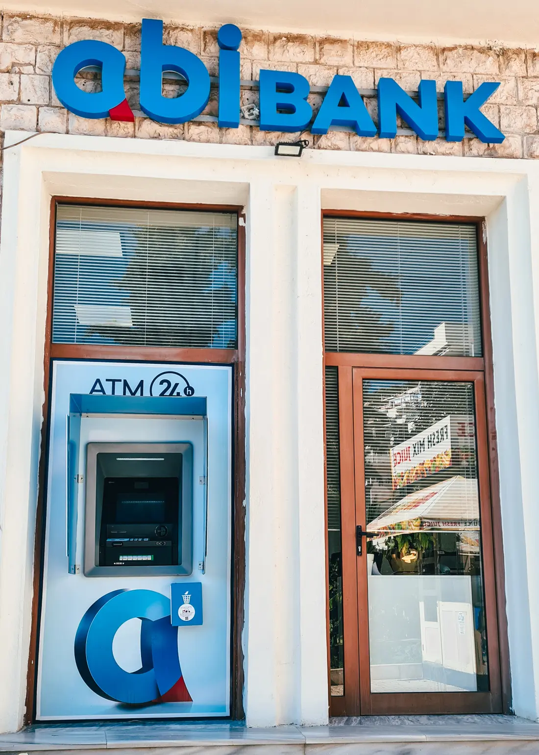 Blue ATM with a large blue OBI Bank sign above and a brown door on the right, the best ATM in Saranda.