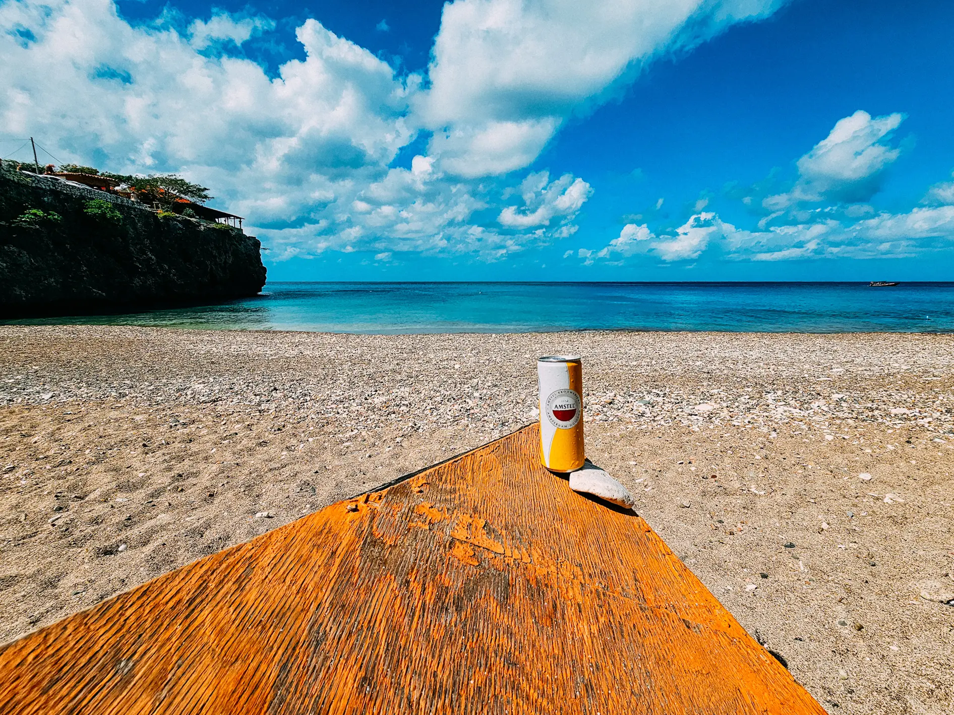 White and yellow beer can on a table by the beach with some clouds on the blue sky, during a private guided tour of Curacao.