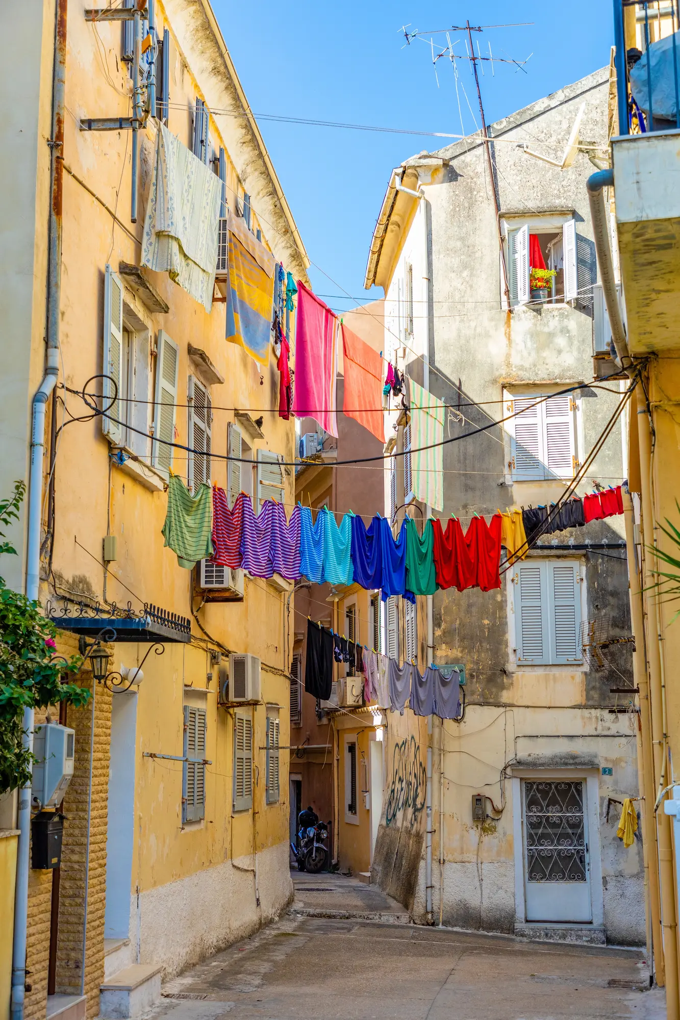 View of a typical alley in Corfu Old Town, with colorful clothes hanging to dry between two old yellow buildings, visiting on a day trip from Saranda by ferry.