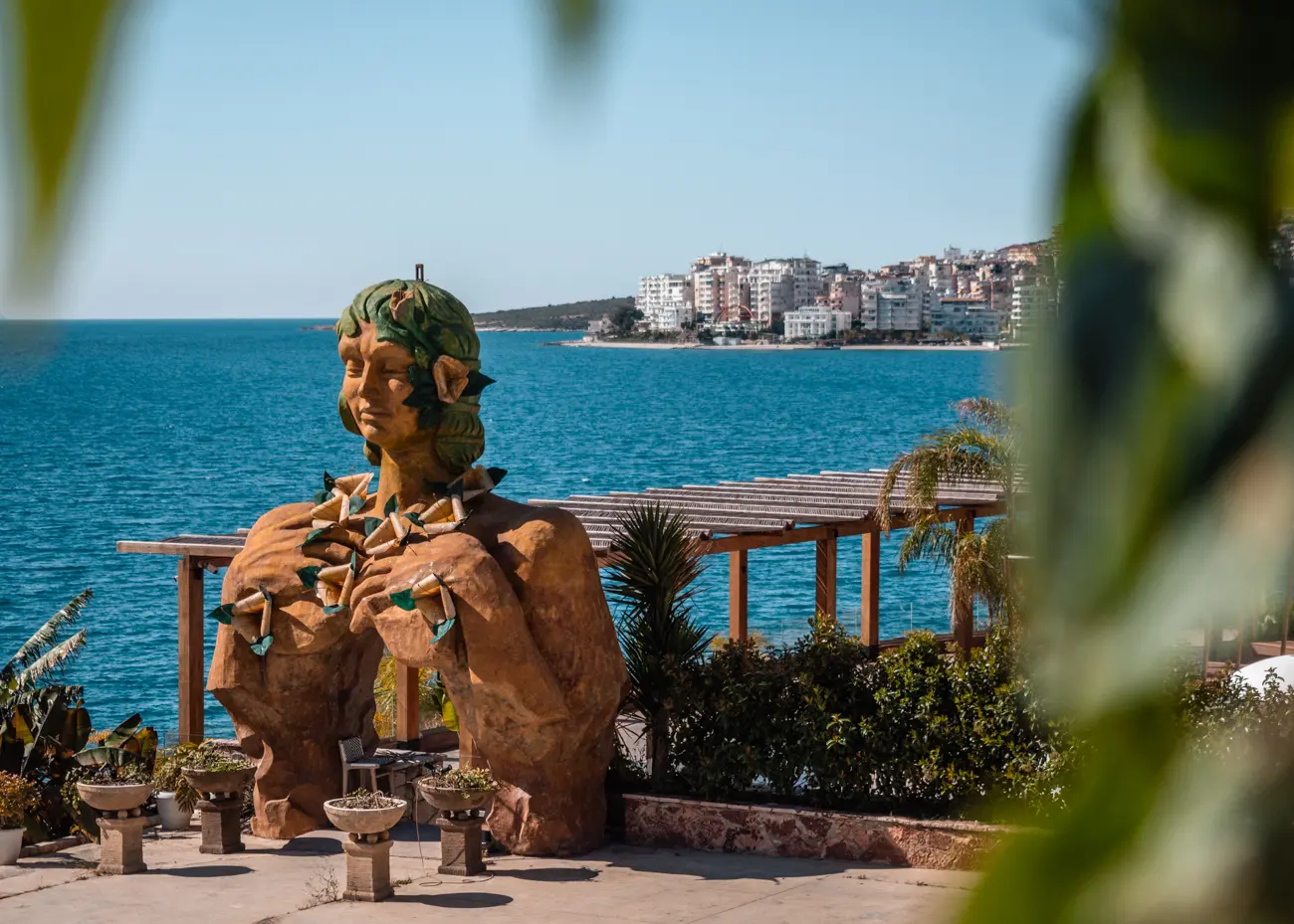 Large brown statue of woman with leaves on her head at the entrance to LOST SEASIDE beach club with blue ocean in the background in Saranda Albania