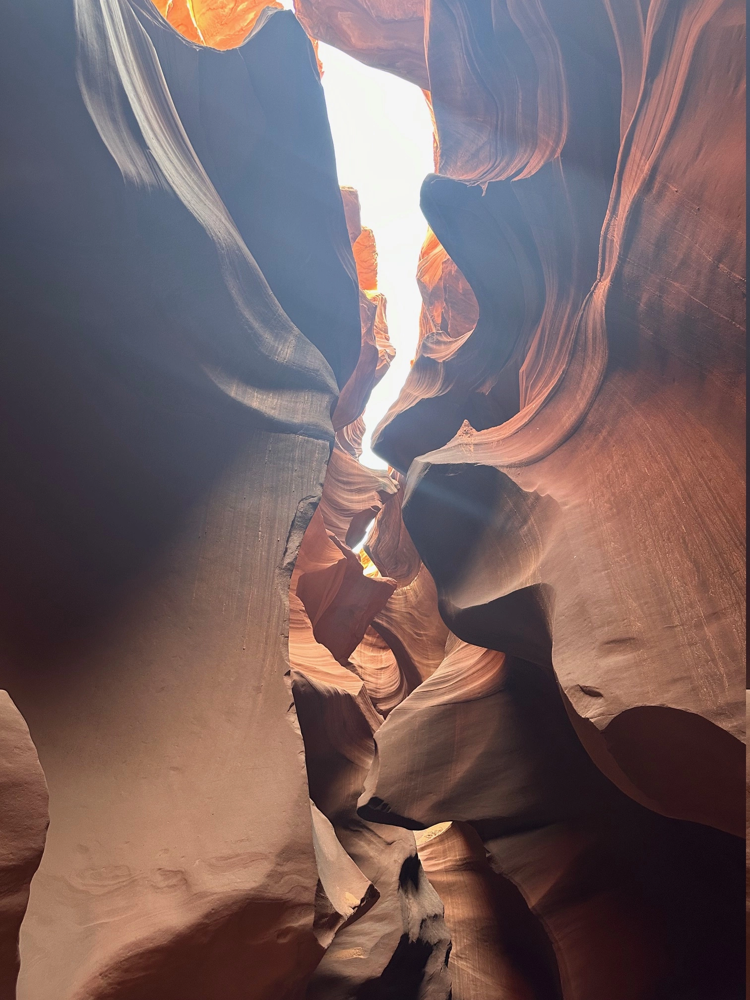 Looking up at the sky through an opening in the brown, wavy sandstone formations on a guide tour of the Lower Antelope Canyon in Arizona.