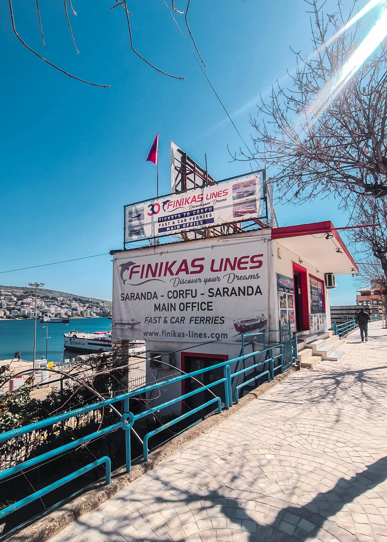 Small white building with red trim and a large Finikas Lines sign on the side next to Saranda to Corfu ferry port.