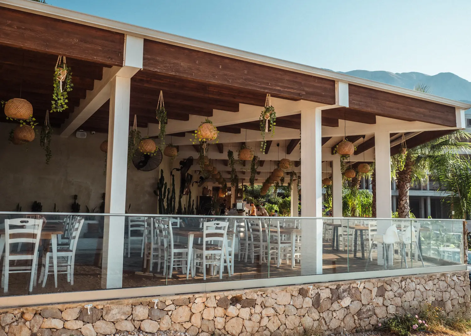 Covered patio of Summer Dream Restaurant with white tables and chairs and plats hanging from the ceiling at Drymades Beach.