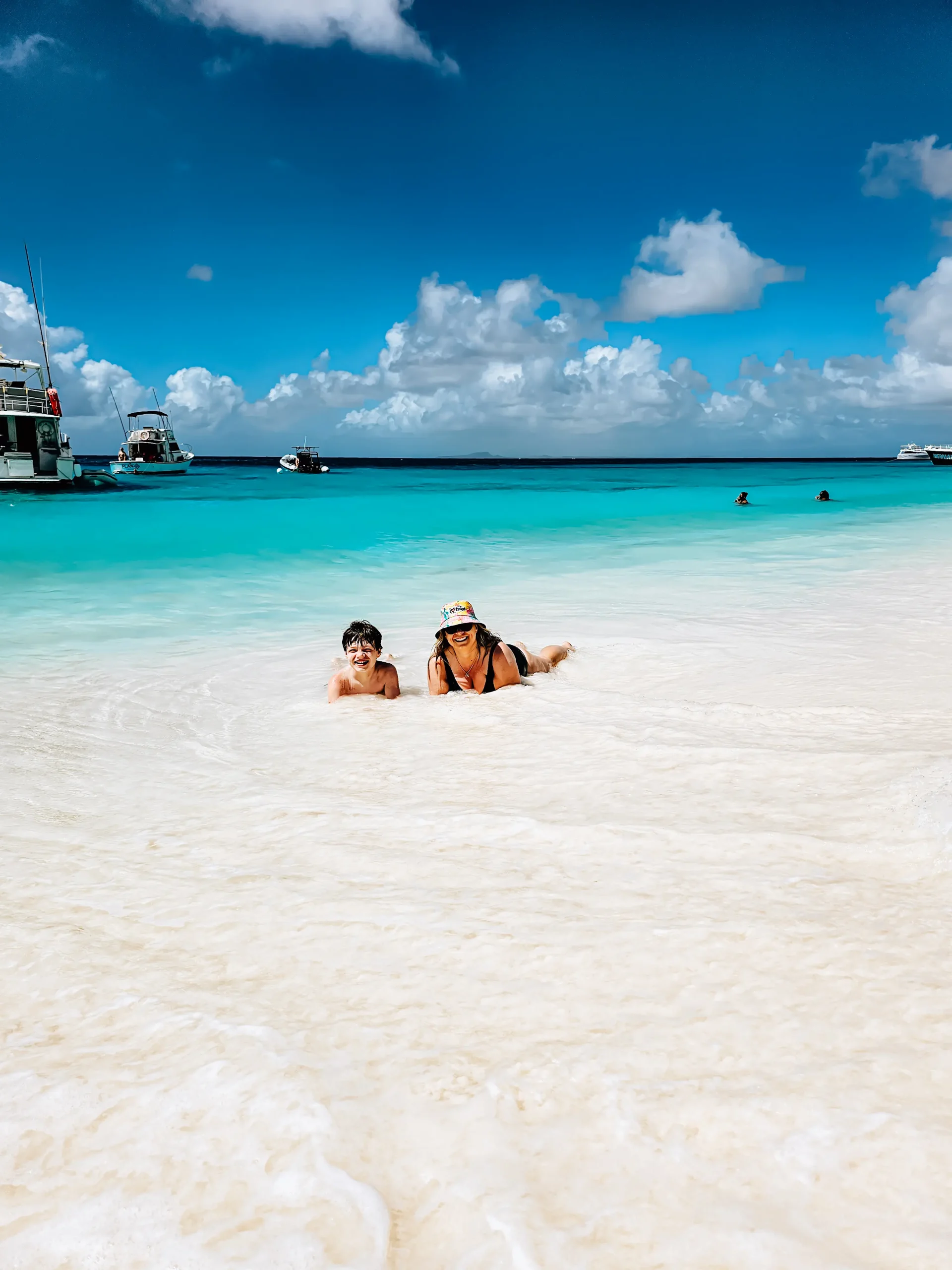 Mom and son lying in the shallows on a white beach with turquoise water in the background, things to know before visiting Curacao.