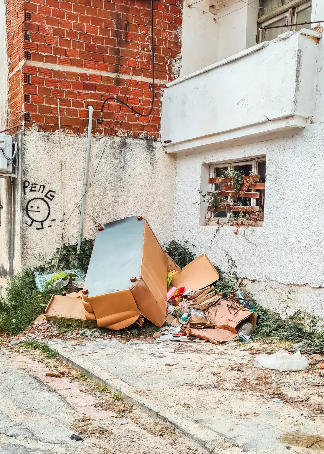 Upside down brown sofa on a pile of trash in a corner outside a shabby white and red brick building in Saranda.