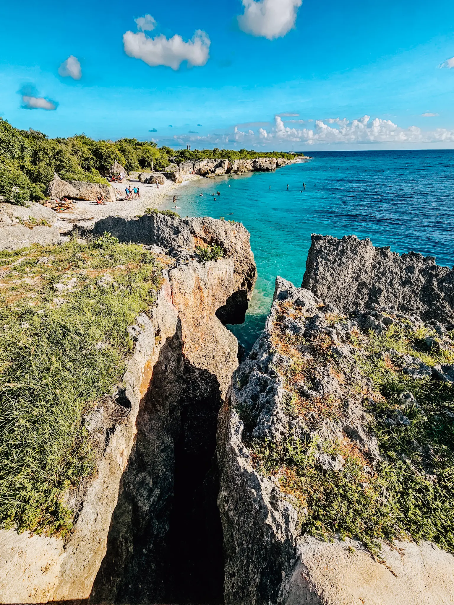 View of Director's Bay Beach and snorkeling spot, seen from a rock formation, surrounded by greenery and turquoise ocean, a Cura&ccedil;ao guide for first-timers.