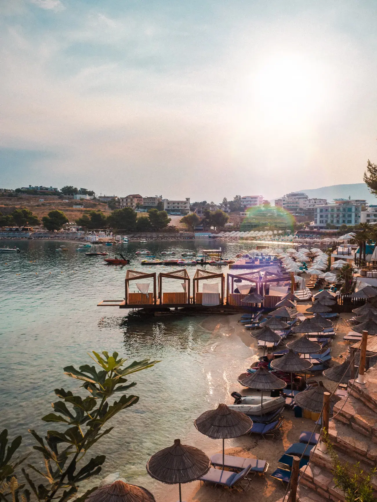 Early morning view of the cabanas and straw parasols on a narrow beach in Ksamil with the sun shining into the camera. Best beaches Ksamil.