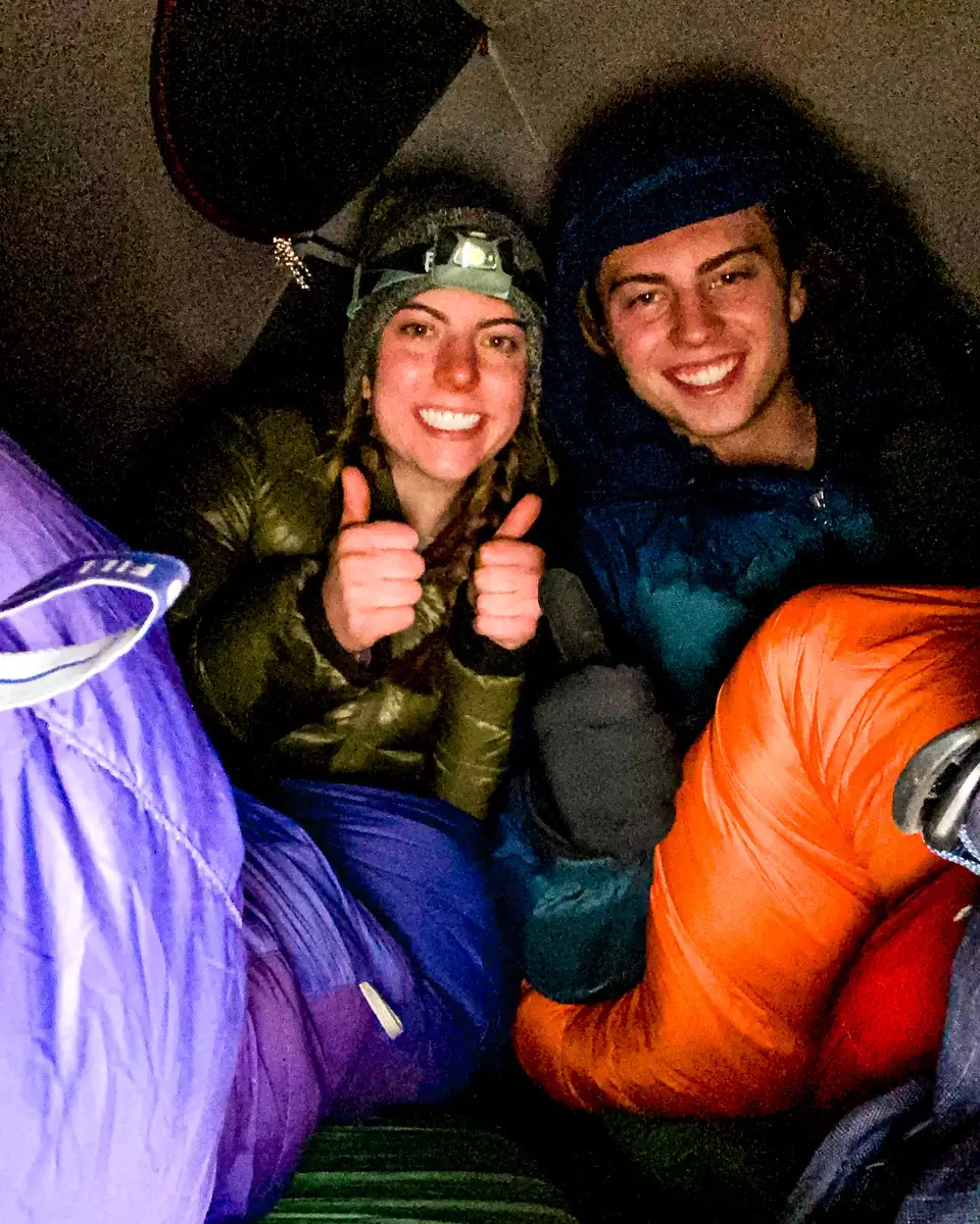 Brother and sister smiling inside a tent at the Barafu Base Camp in purple and orange sleeping bags, while hiking Kilimanjaro.