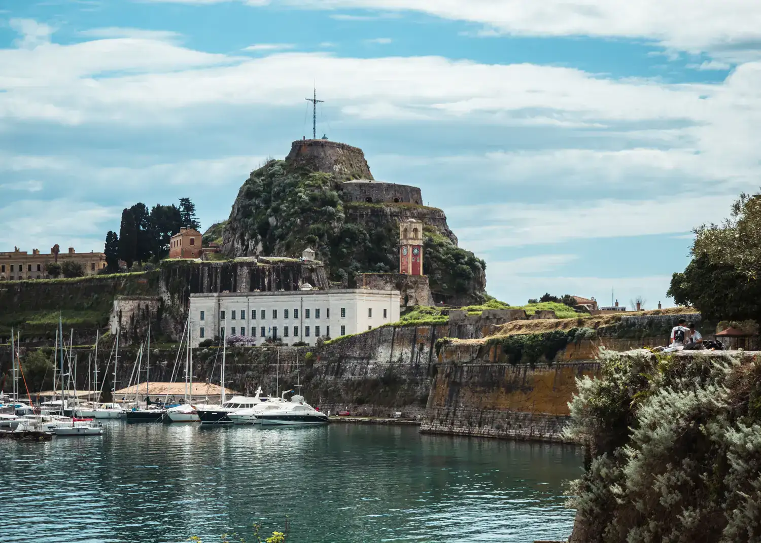 View of the Old Fortress on a headland in Corfu Town, with a cross on top, white sailboats next to it, seen during a one day in Corfu Old Town.