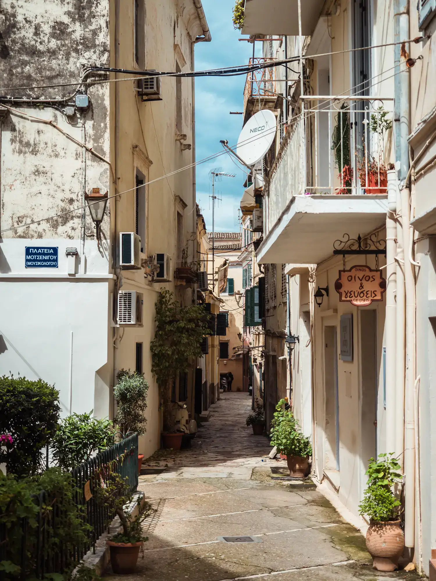 Paved alley between two light colored buildings in Corfu Old Town.