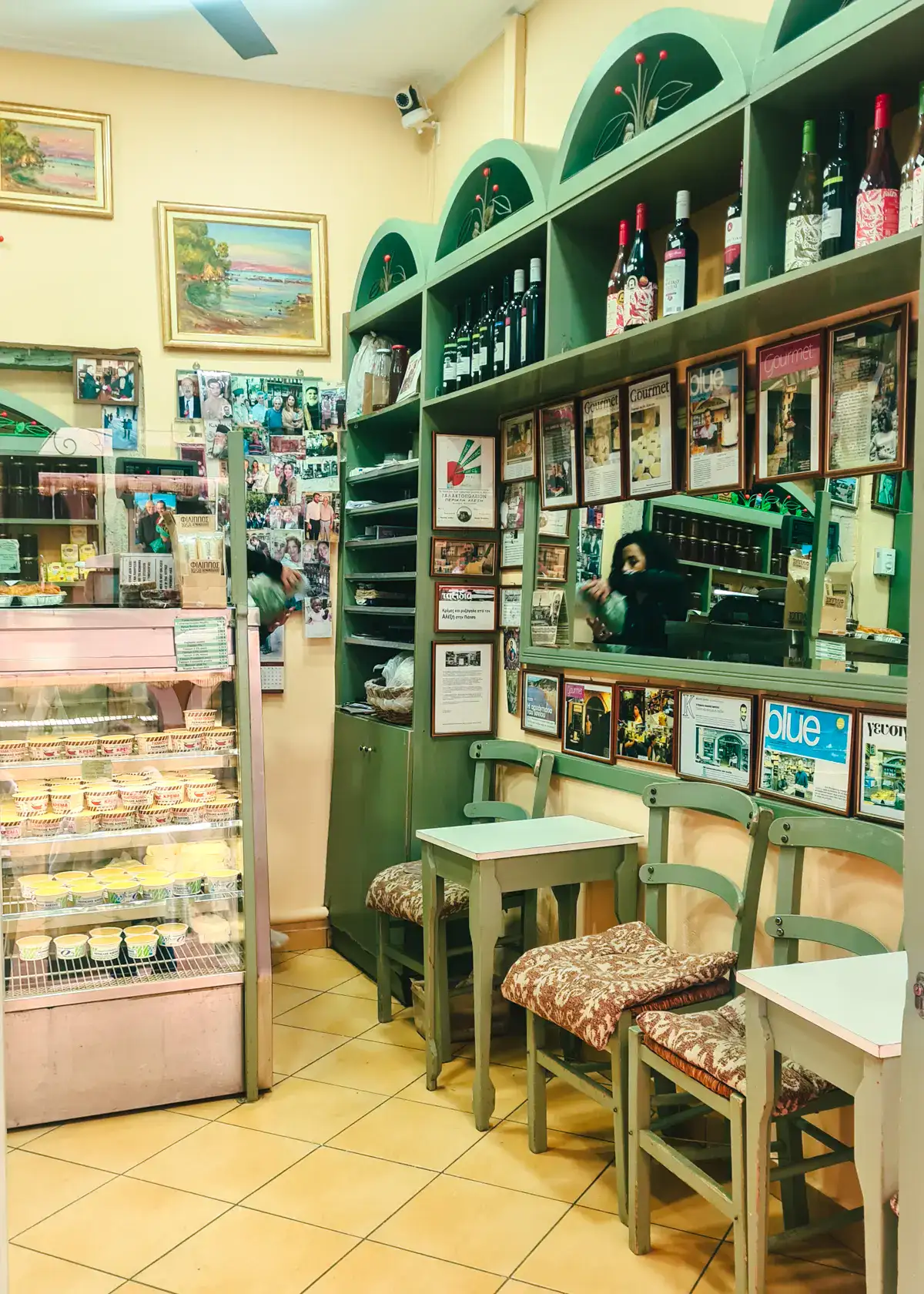 Looking into the traditional Alexis Dairy Shop in Corfu Old Town, with a glass counter full of butter and green shelves on the right with a mirror and different news articles.