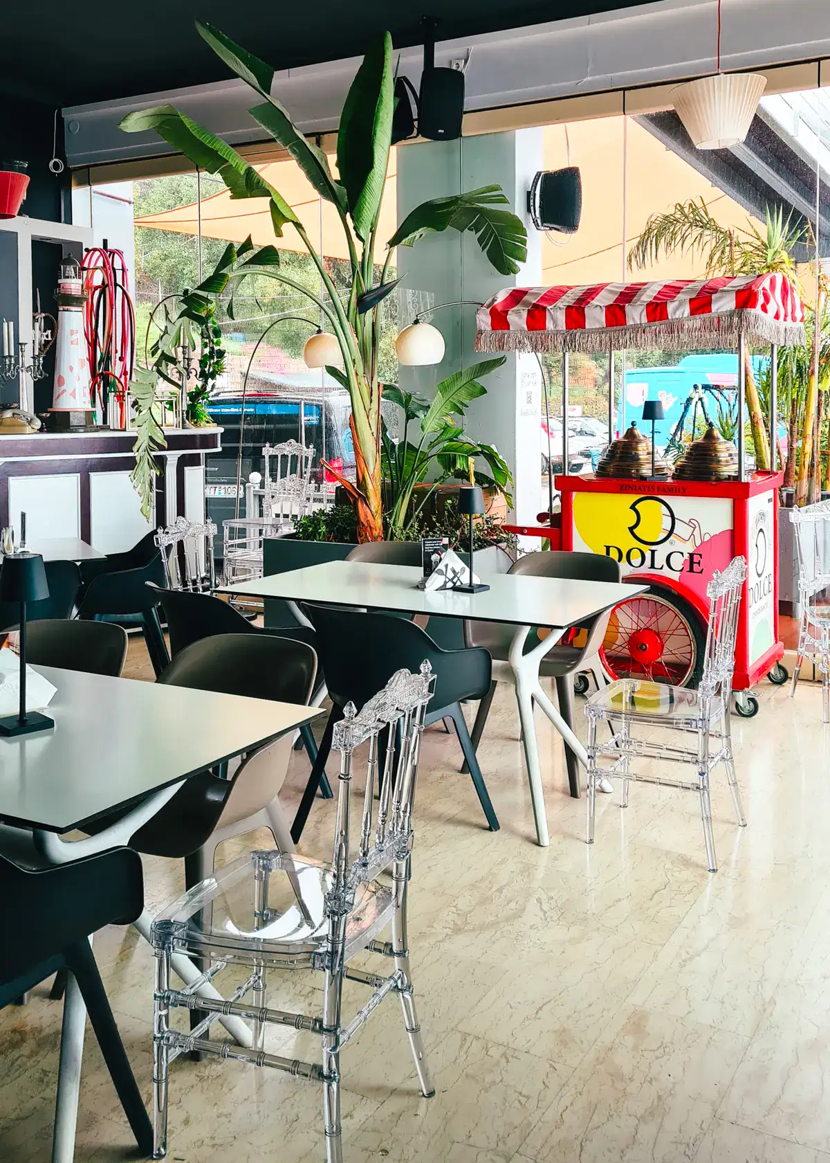Two grey tables with black and clear chairs with a carnival looking one cream cart in Dolce Café in Lakones Village, during a Corfu day tour.