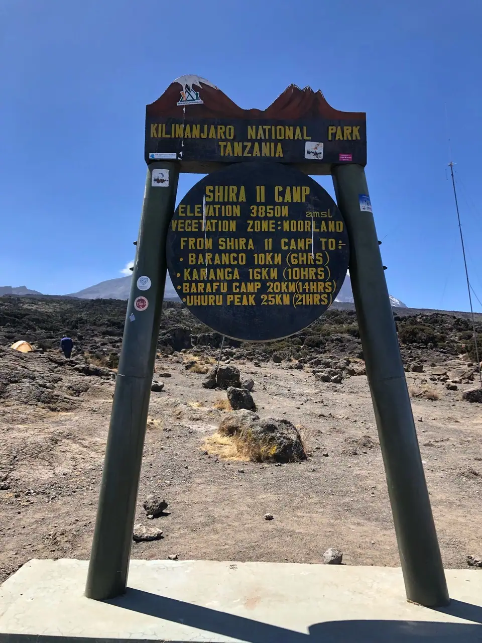Metal mount with round Shira Camp II sign on a sunny day on the way to the summit of Mount Kilimanjaro.