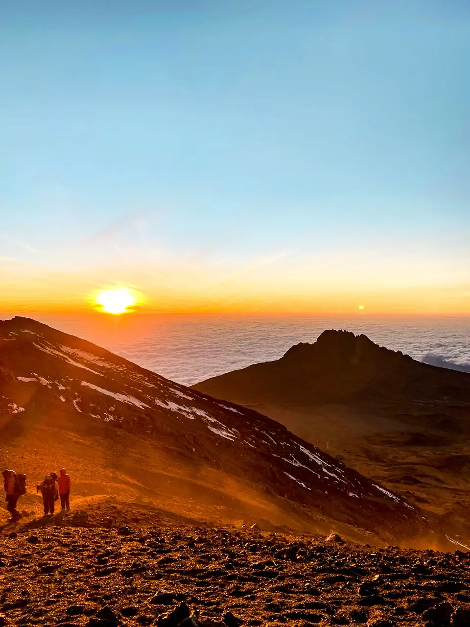 Blue and orange sunset view of people hiking up Mount Kilimanjaro above the clouds.