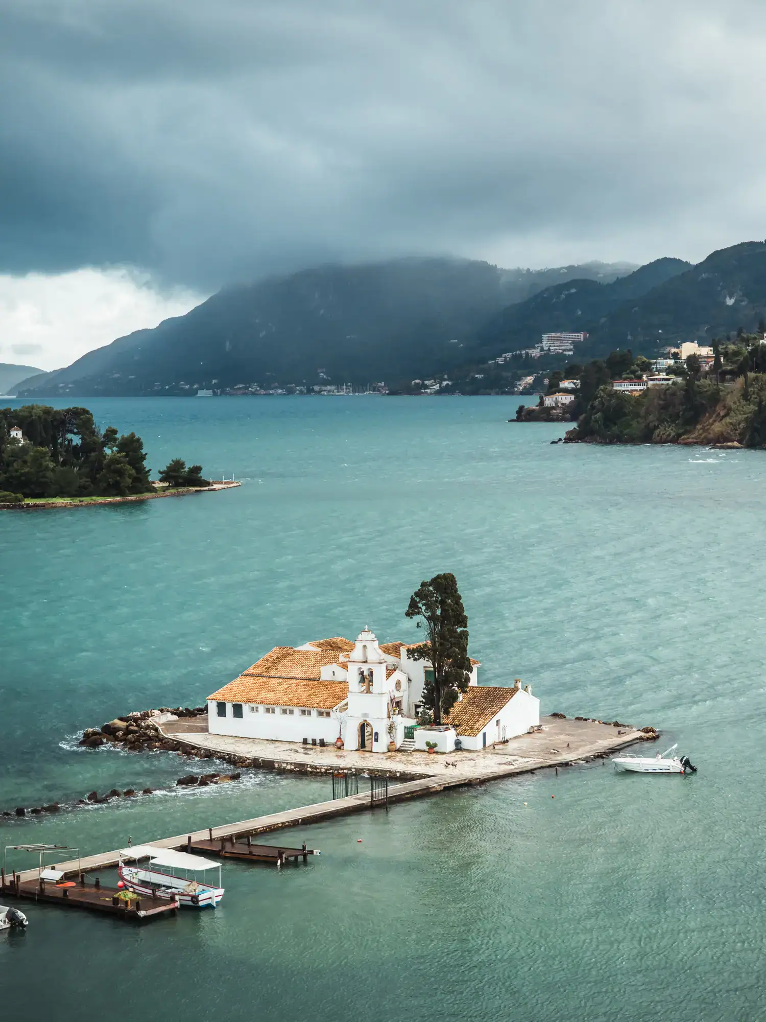 White Vlacherna Monastery on a small island, surrounded by light blue ocean on a stormy day, seen from Kanoni Viewpoint during a one day itinerary.