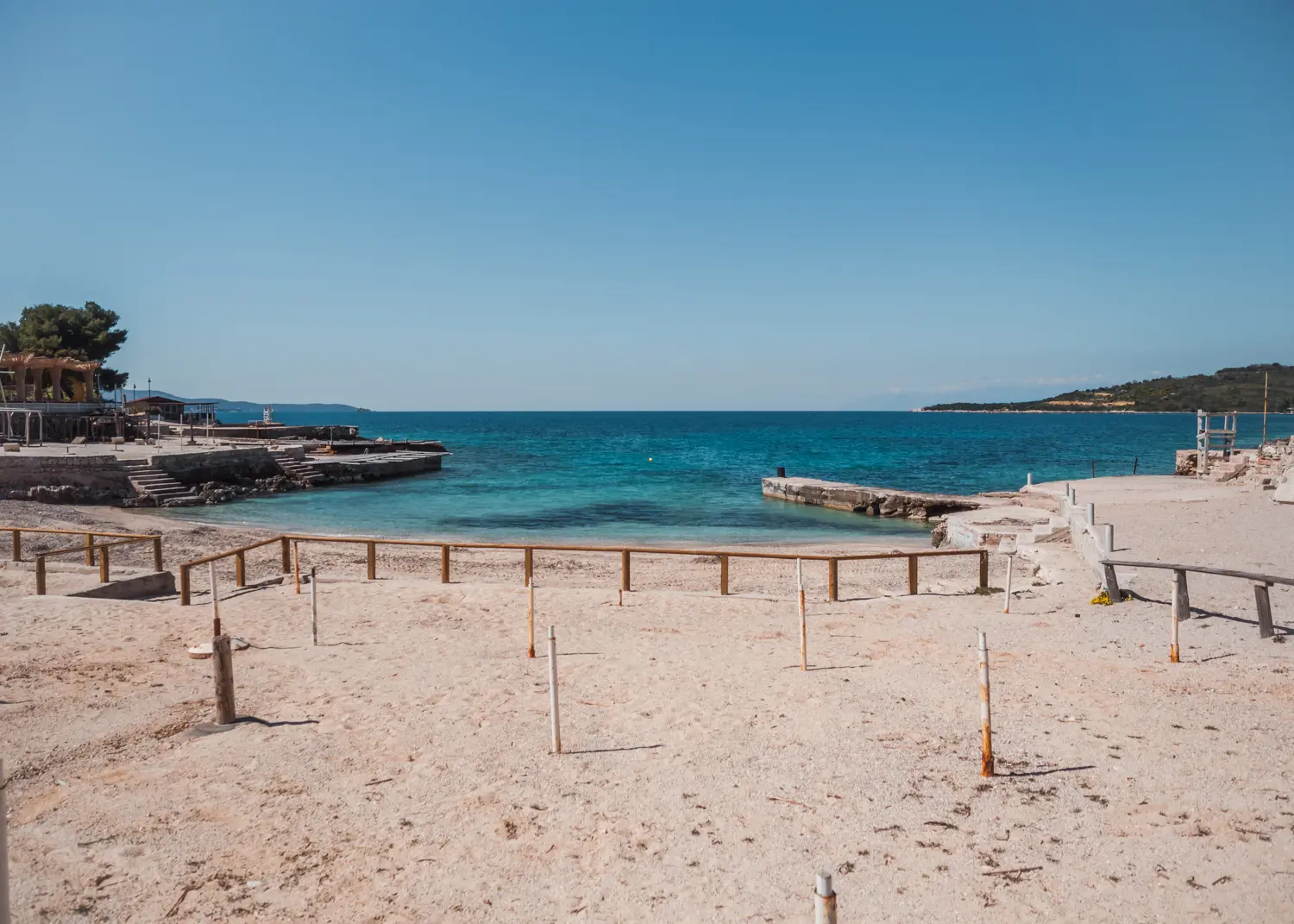 Small beach with a small wooden fence and spikes for umbrellas by the blue ocean, Ksamil Beach guide.