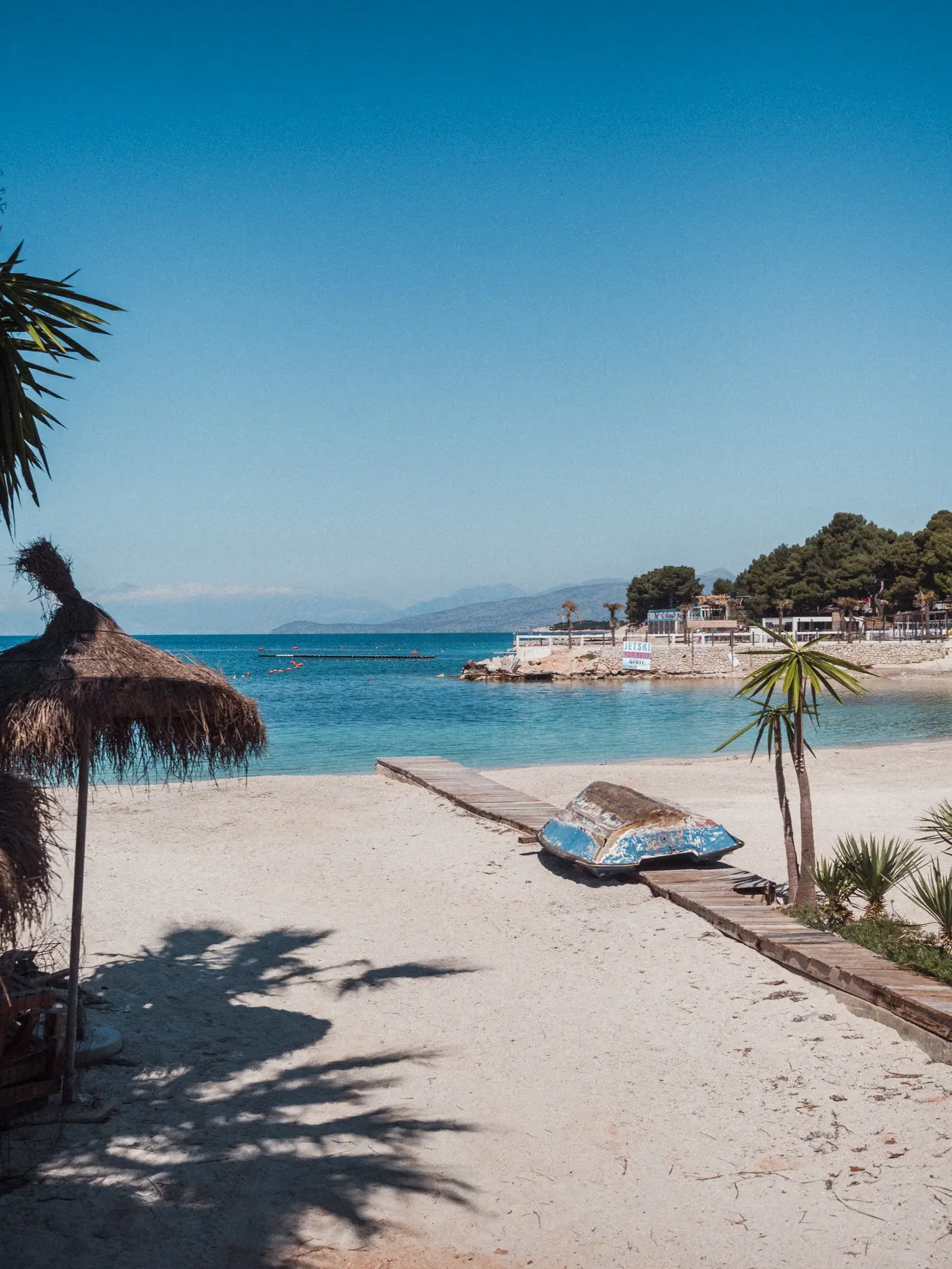 Old, blue boat on a wooden walking track going across Poda Beach, the most popular beach in Ksamil.