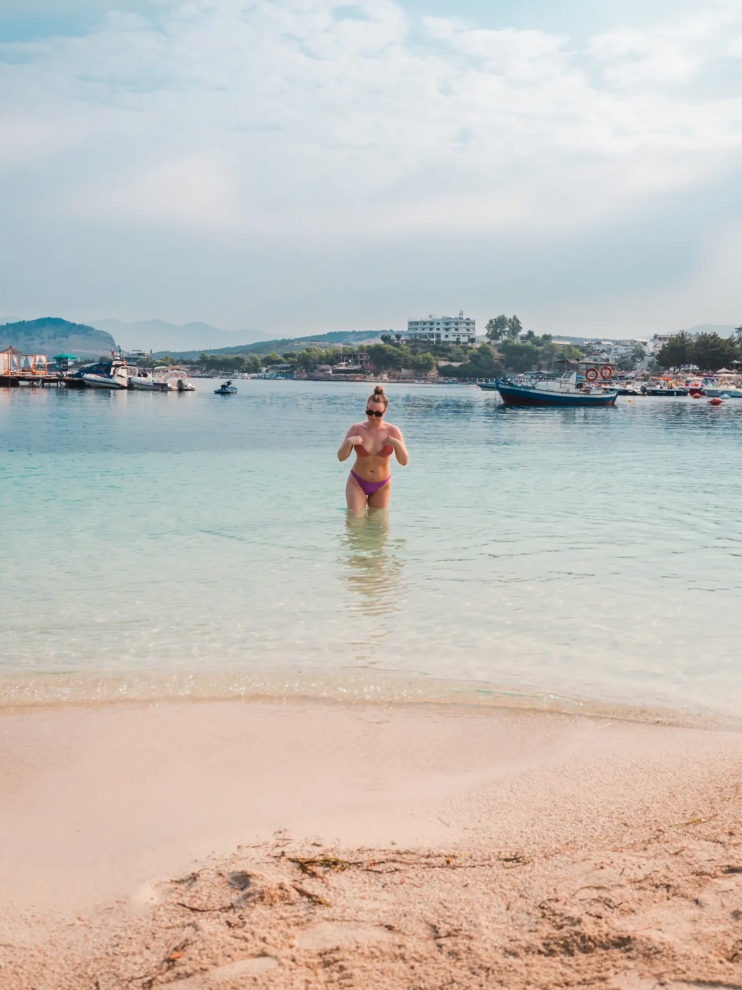 Woman wearing a purple bikini walking out of the clearwater on Lori Beach in Ksamil.