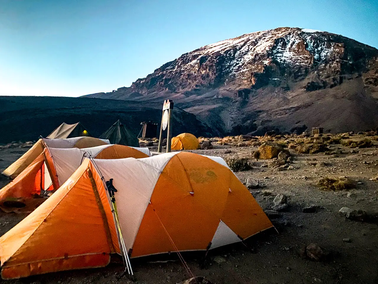Three white and orange tents with Mount Kilimanjaro in the background, at one of the campsites while hiking Kilimanjaro, this is what you need to know.