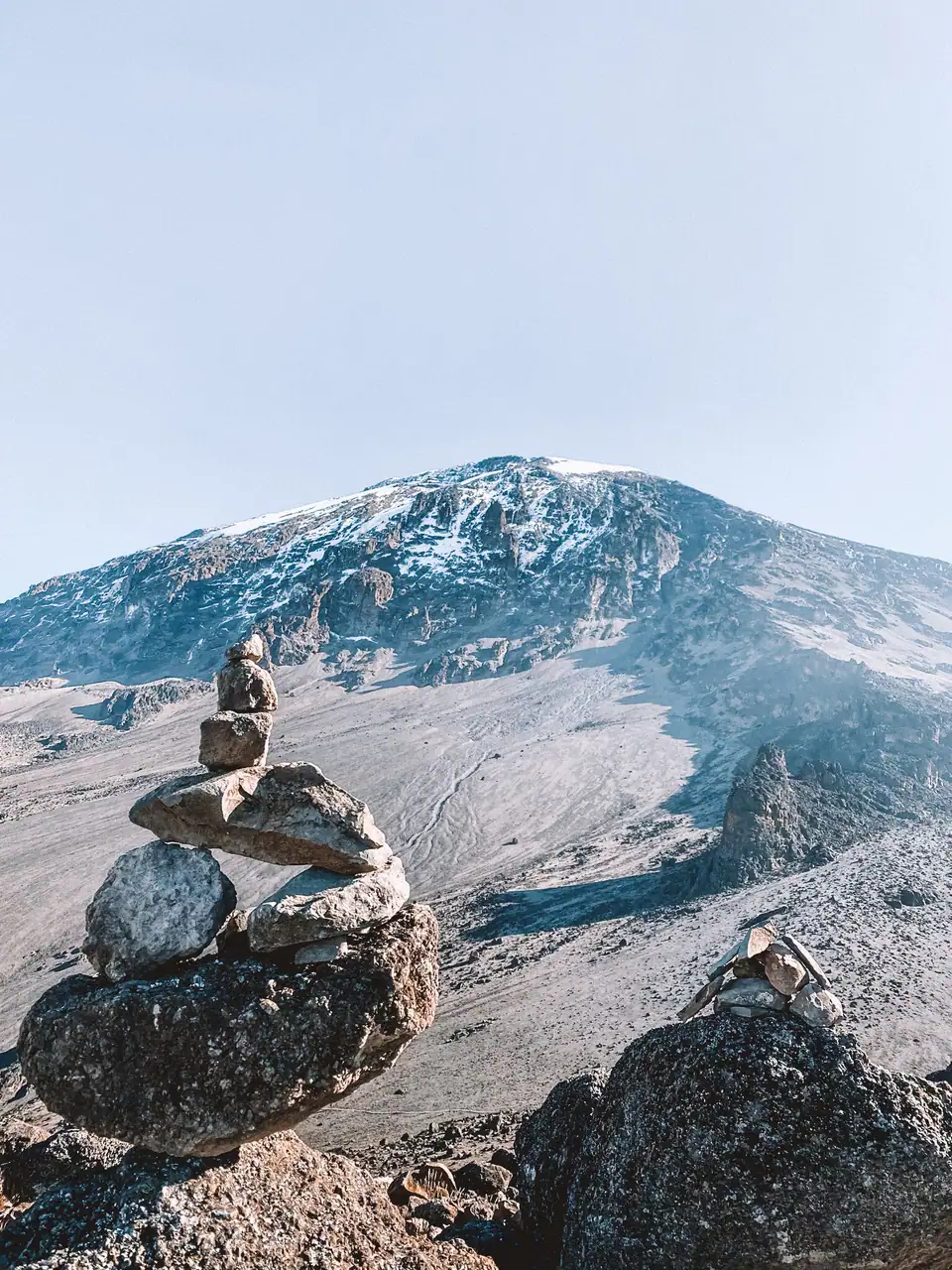 Stones stacked on top on each other with Mount Kilimanjaro in the background in the early morning light, during a 8-day Kilimanjaro hiking itinerary.