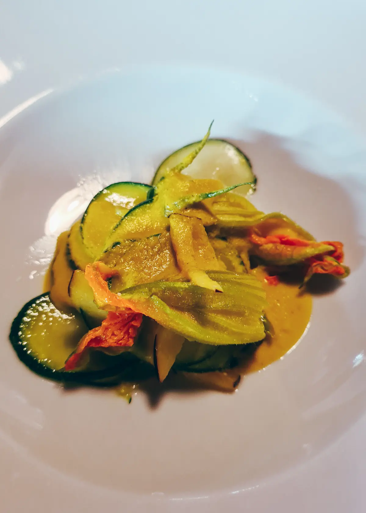 Zucchini and zucchini flower salad with a light orange vinaigrette in a white bowl at Mullixhiu in Tirana.