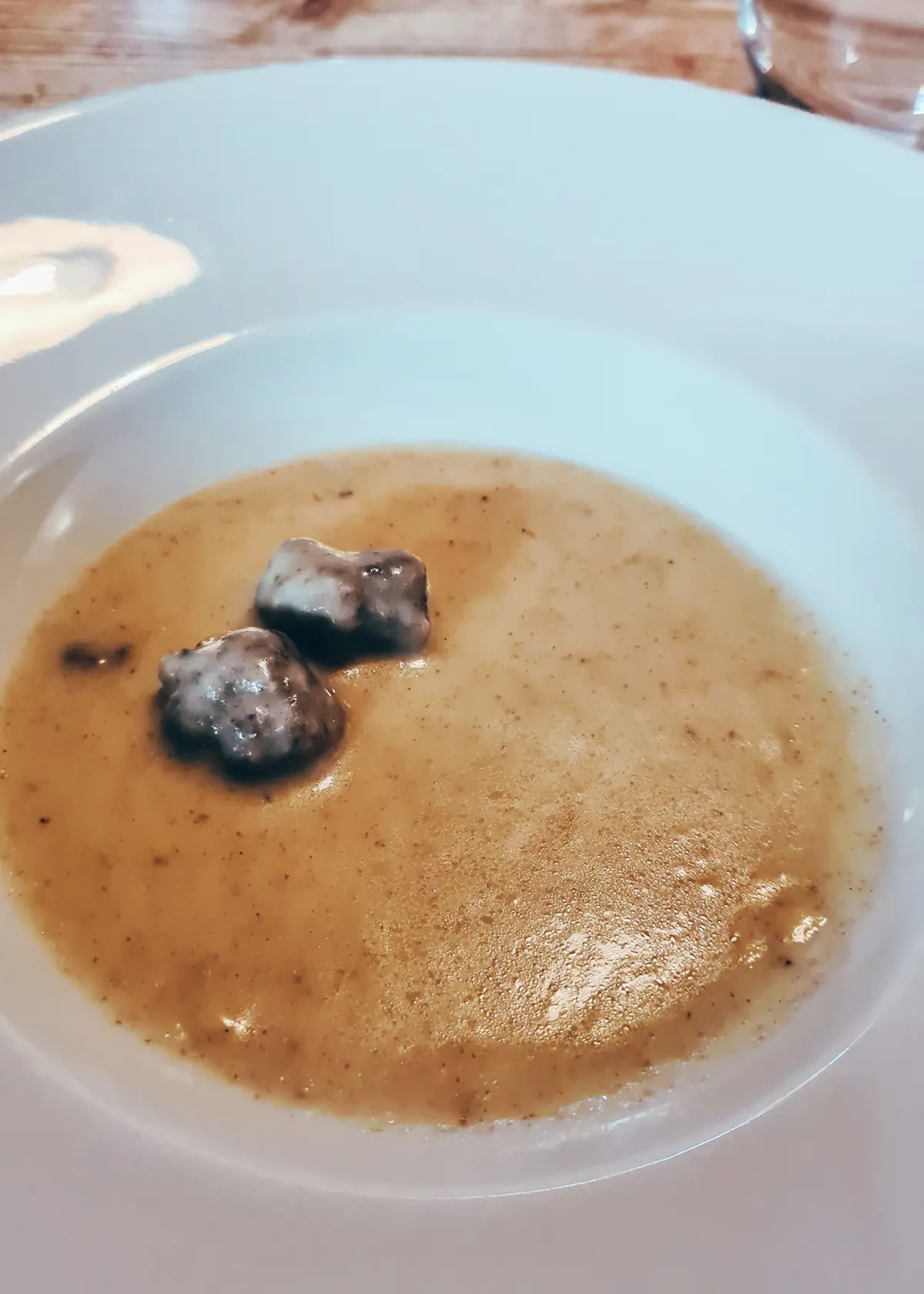 Light brown grain soup with two small meat balls in a white bowl, during a 7-course dinner at Mullixhiu restaurant in Tirana, Albania.