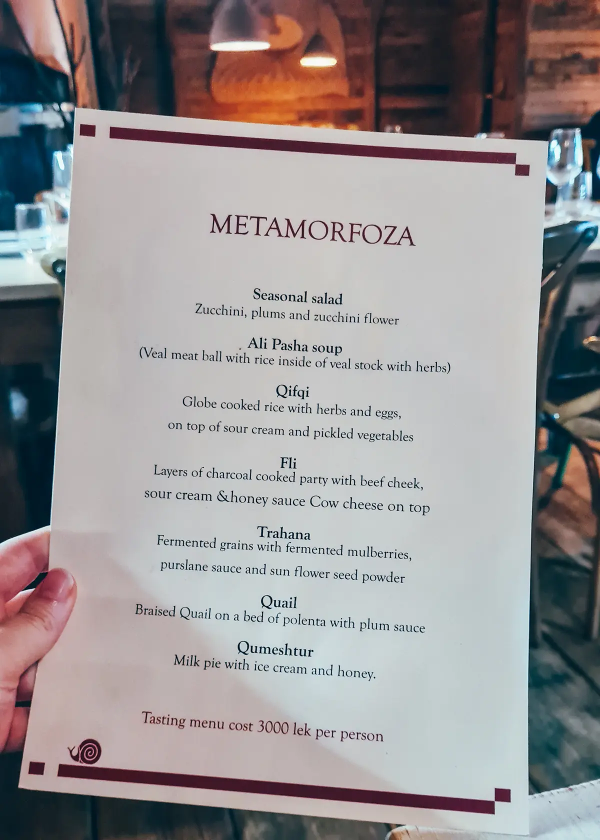 Hand holding a white menu explaining the 7-course menu at Mullixhiu Restaurant in Tirana, Albania.