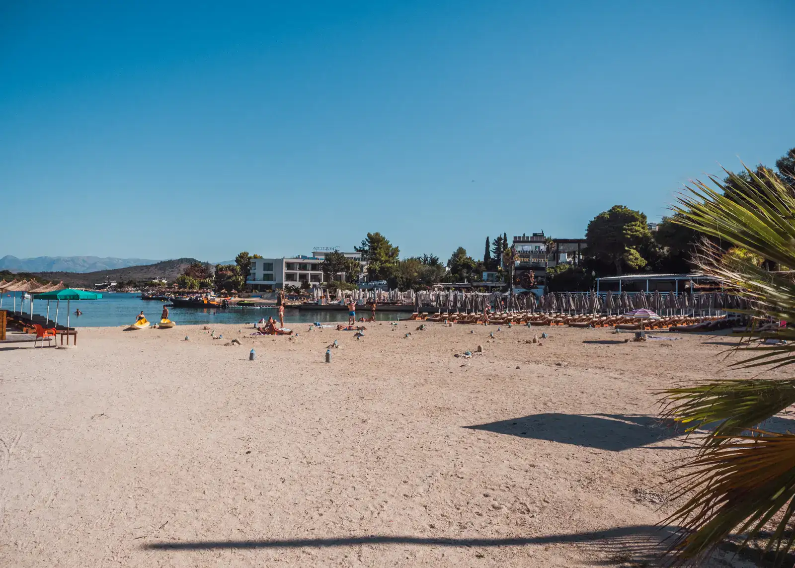 The public area of Paradise Beach with a few people and sunbeds in the background on a sunny day in Ksamil.