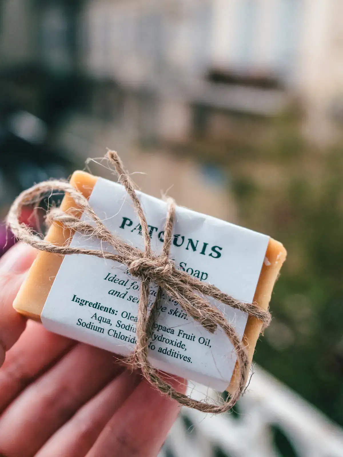 Close up of hand holding an olive oil soap wrapped in a white label with brown string in a bow, from the Patounis Factory in Corfu Old Town.