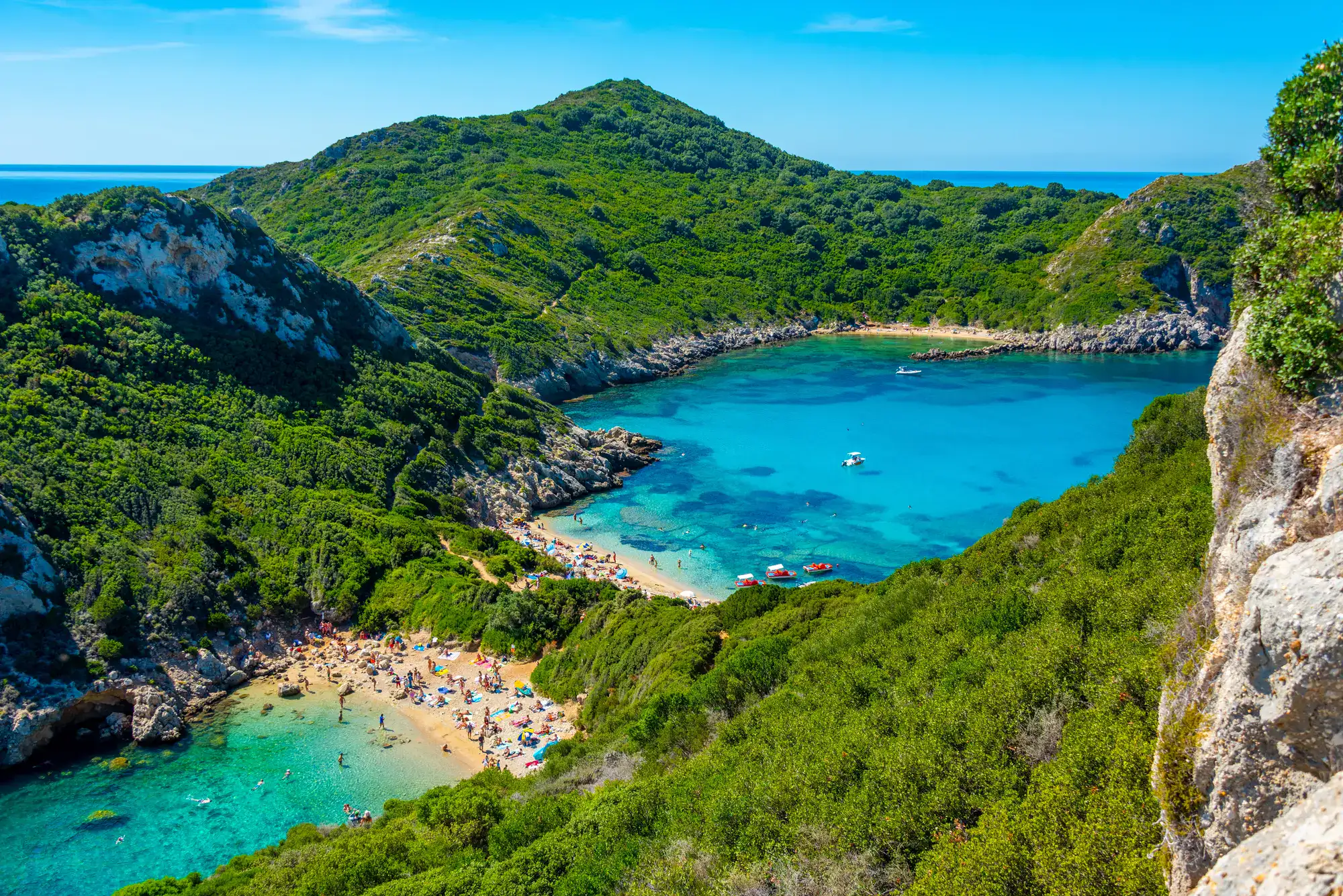 View of Porto Timoni Beach set on two sides of a narrow outcrop, surrounded by green rocks and mountains, and  turquoise ocean, a must on any Corfu itinerary.