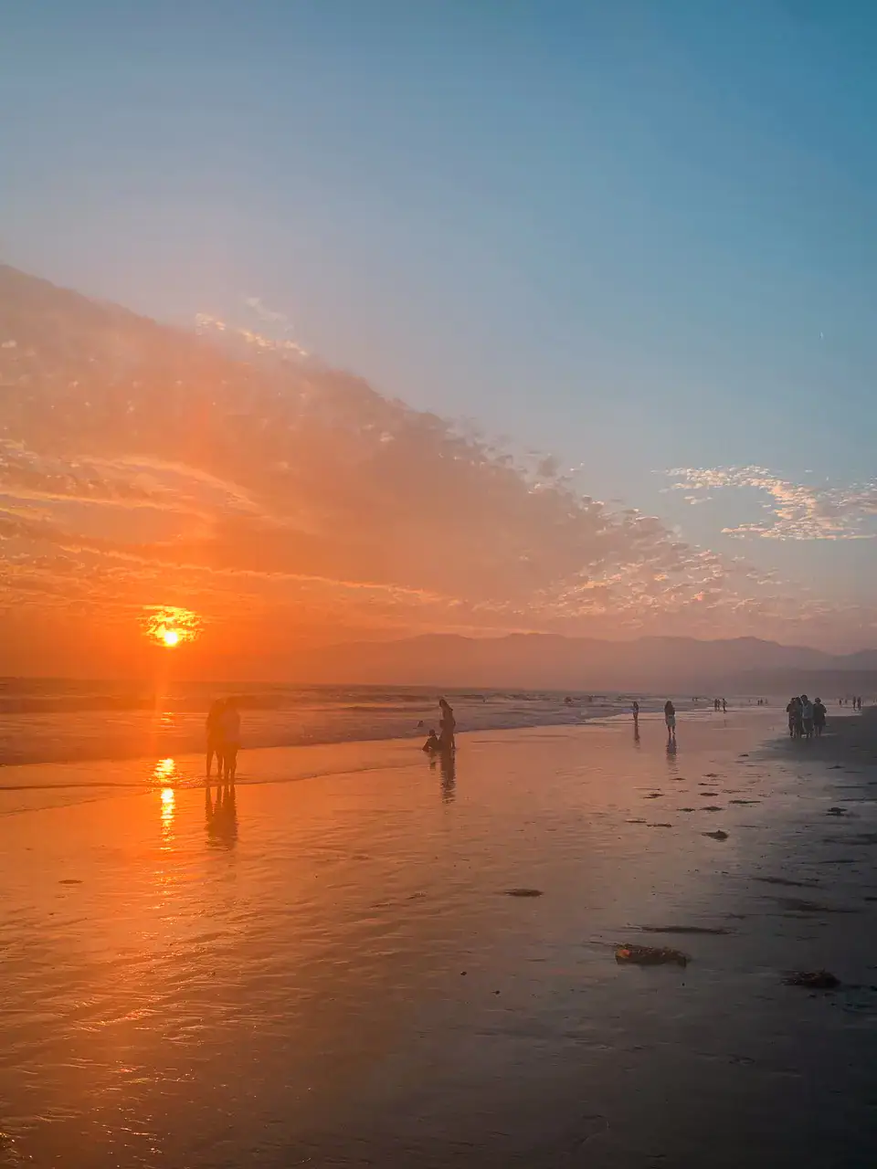 People walking along the shore on Santa Monica Beach during an orange sunset, Los Angeles Itinerary.