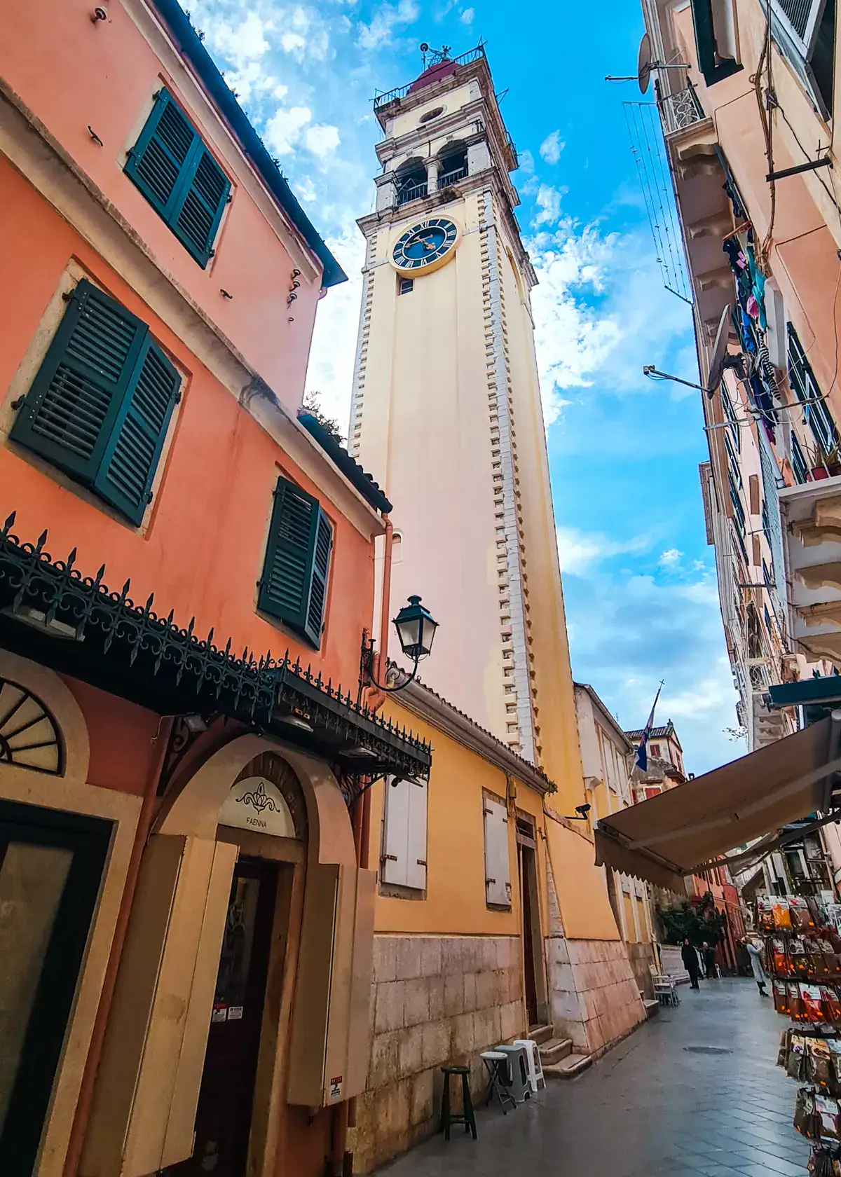 View of the yellow, narrow tower of the Church of Saint Spyridon, taken from a narrow alley with the blue sky in the background in Corfu Old Town.