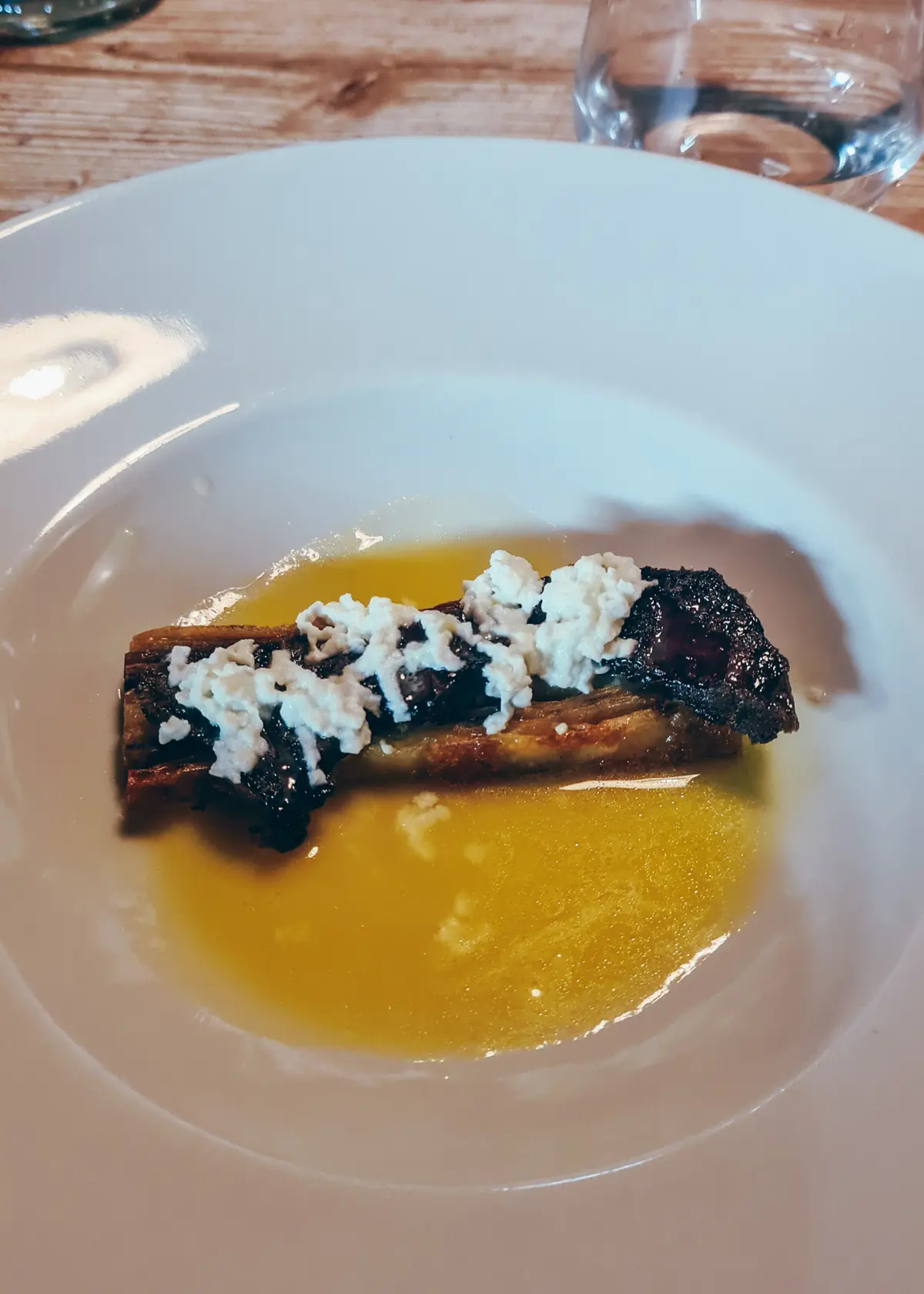 Thins slice of layered pastry topped with slow coked beef cheek and cheese in a honey sauce, served on a white plate at Mullixhiu in Tirana.