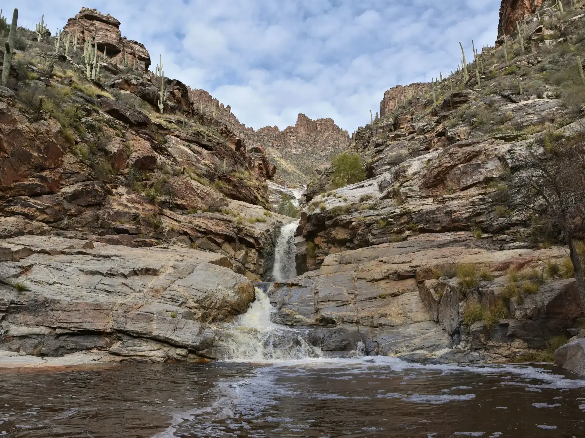 The narrow Seven Falls running into a pool at the bottom of two cliffs on a partly cloudy day, close to Tuscon on a day trip from Phoenix.