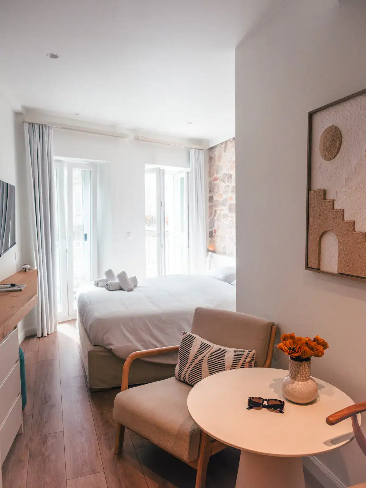 Looking into the bedroom of my apartment rental in Corfu Old Town, two chairs and white table, beige and brown art on the wall, two doors at the end of the room.