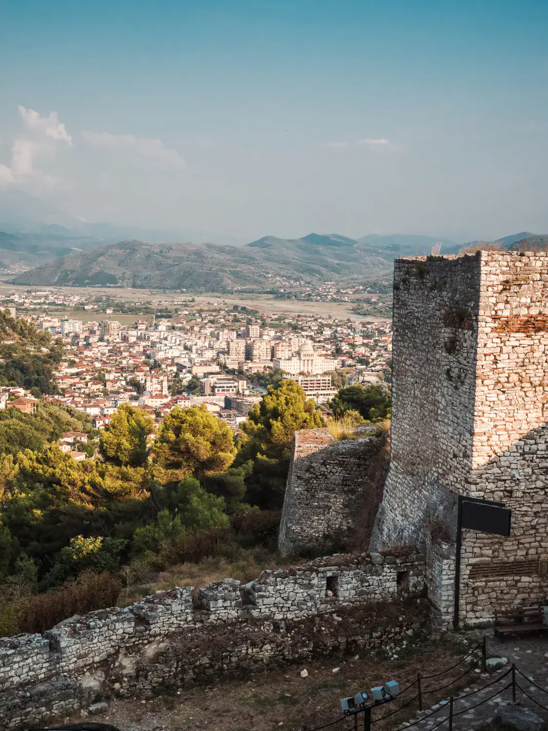 Looking past a ruin stone tower at Berat Castle down on the new part of Berat Albanian at sunset.